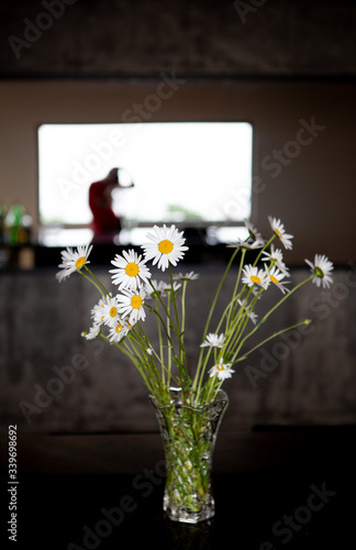 Daisies in a glass pot on top of a black quartz counter in front of a mirror