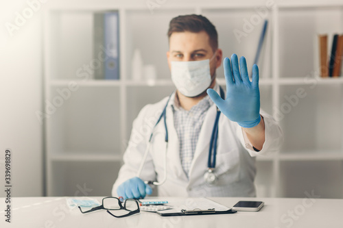 Portrait of doctor in medical uniform with a protective face mask and a gloved hand showing a stop sign. Stop COVID-19 concept.