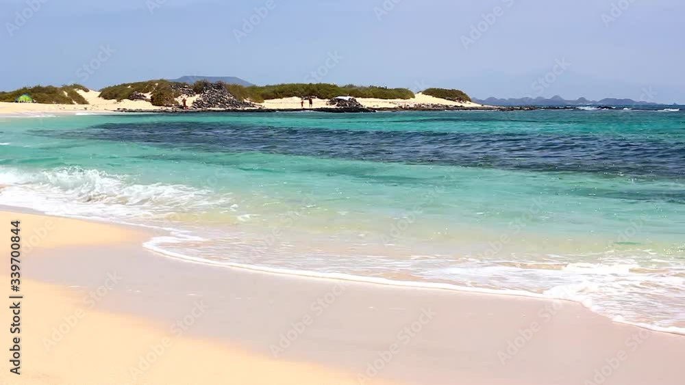 Corralejo empty beach with turquoise water on sunny day in Fuerteventura. Waves on shore of transparent sea in Canary Islands, Spain. Summer travel destination, paradise concepts Corralejo empty beach with turquoise water on sunny day in Fuerteventura. Waves on shore of transparent sea in Canary Islands, Spain. Summer travel destination, paradise concepts