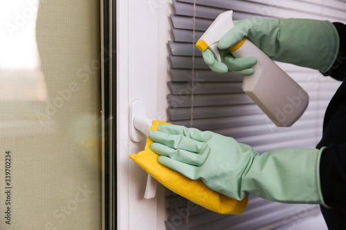 Φωτογραφία cleaner's hands in rubber green gloves doing disinfection cleaning door handle with detergent spray and rag