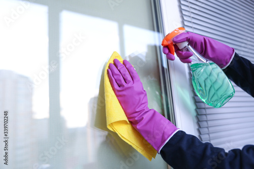 cleaning company worker cleans window with cloth and spray cleanser photo