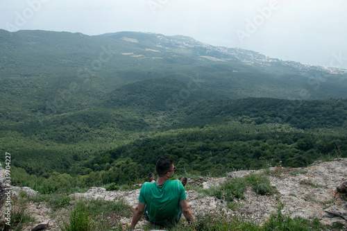 Young man sitting on vertex and looking at natural beauty - fresh air, hills, pacifying landscape