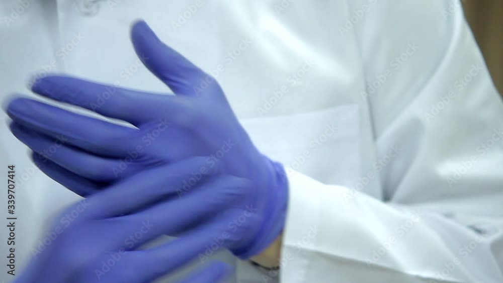 A doctor in a white medical coat puts on purple rubber gloves, close-up. A doctor in a white medical coat puts on purple rubber gloves, close-up.