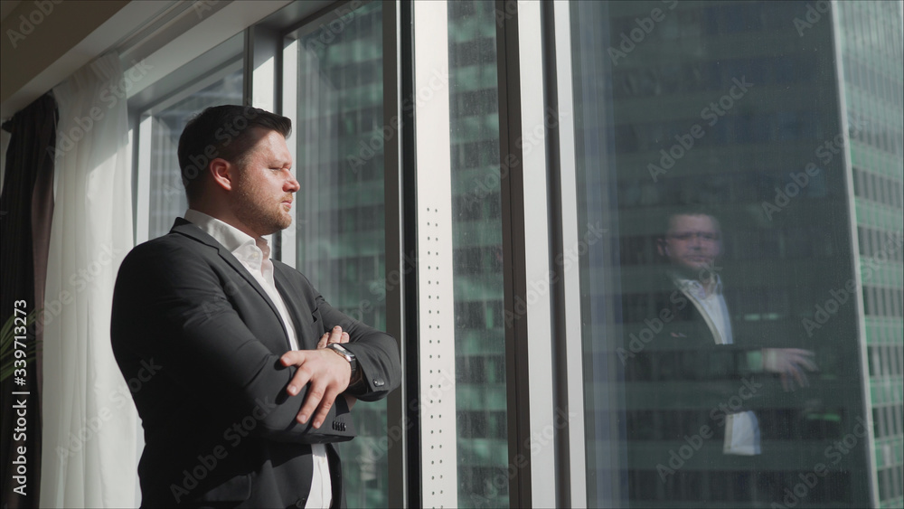 A businessman goes to the window. Side view on Handsome businessman in suit walking outdoor big glass urban airport building. Successful businessman in his office with panoramic windows. A businessman goes to the window. Side view on Handsome businessman in suit walking outdoor big glass urban airport building. Successful businessman in his office with panoramic windows.