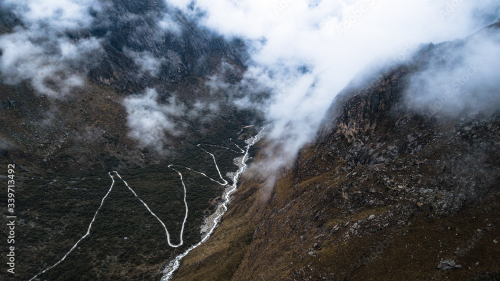 Aerial view on zig zag mountainous road through the valley next to the river and clouds passing by the valley at 4600m above the sea level, Cordillera Blanca, Huascaran National Park, Peru.