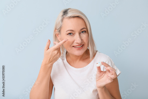 Mature woman putting in contact lenses against light background