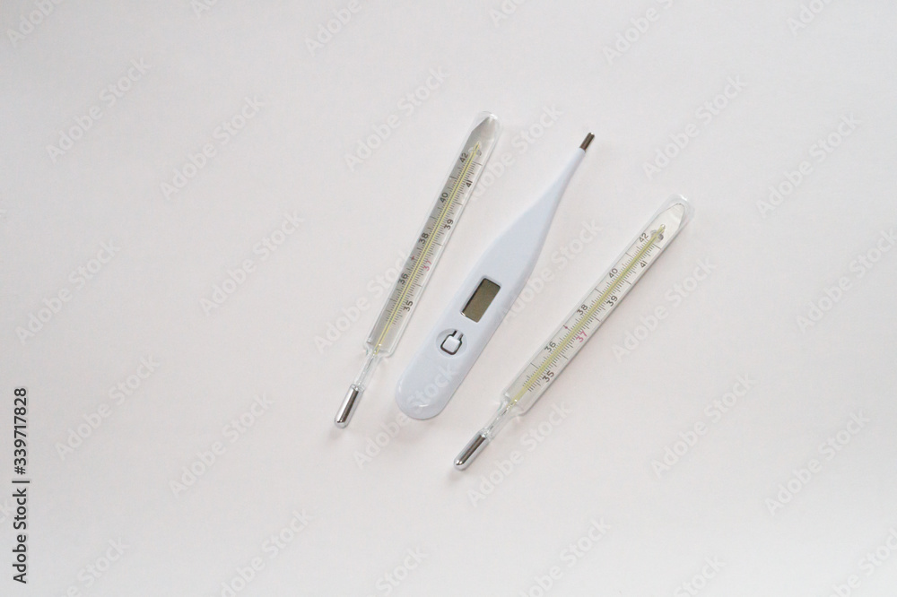 One white digital electronic thermometers and two analog mercury thermometers on a white background One white digital electronic thermometers and two analog mercury thermometers on a white background