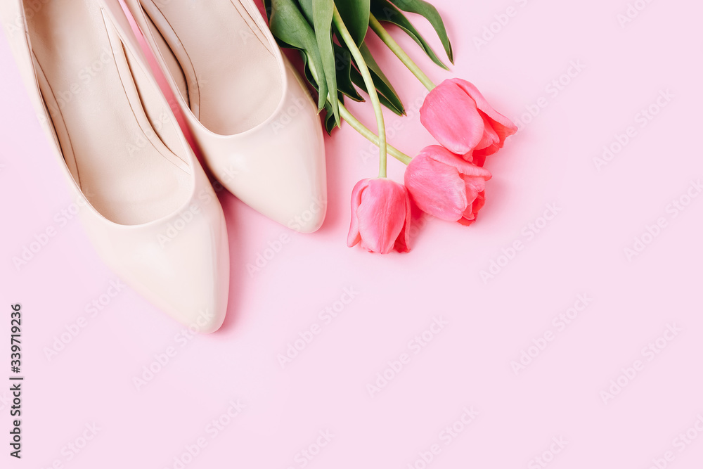 Female high-heeled shoe with beautiful tulips on pink background