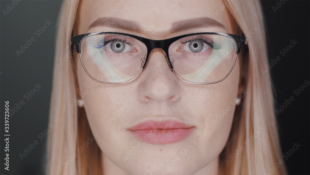 Fototapeta premium Attractive blonde hair business woman in glasses is looking at camera and smiles to show teeth braces standing at black background. Orthodontic treatment concept. Slowmotion closeup portrait 4K video