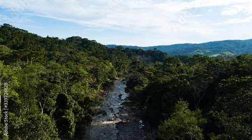 Aerial view on a river crossing the amazon rainforest in the Peruvian jungle. Stones in the river, green trees, blue sky, full vegetation. 