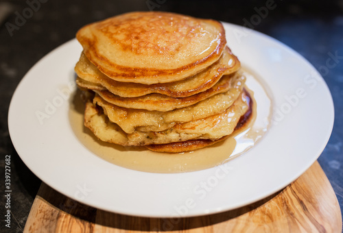 Fresh homemade classic pancakes with maple syrup in a white plate on a wooden board.