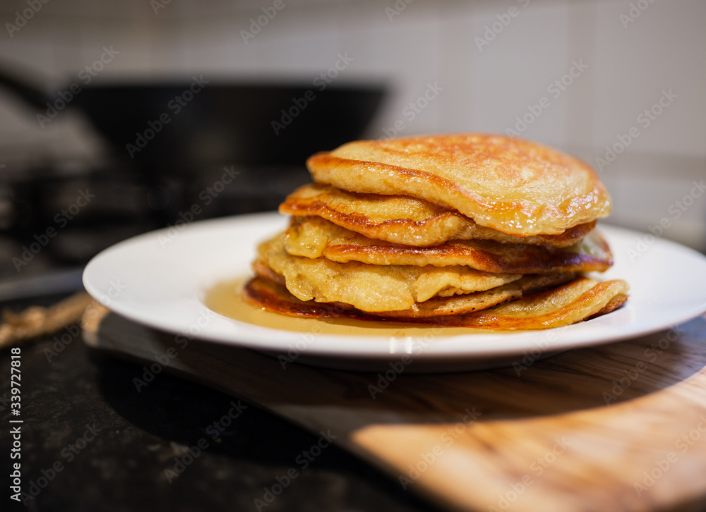 Fresh homemade classic pancakes with maple syrup in a white plate on a wooden board with a pan in the background. Fresh homemade classic pancakes with maple syrup in a white plate on a wooden board with a pan in the background.