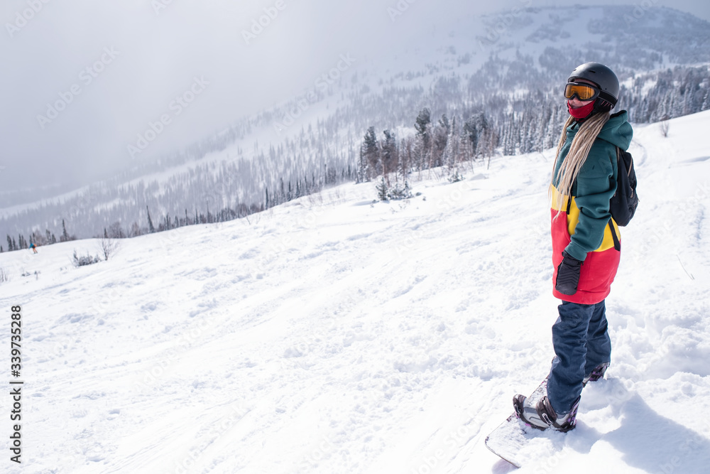 Young woman with snowboard in the mountains walking on a snowy slope.