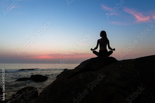 Silhouette of yoga woman sit at Lotus position on the shore of ocean at amazing twilight.