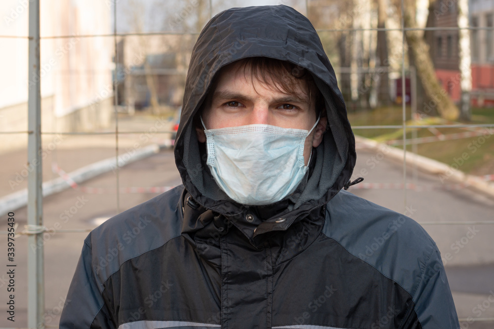 Close-up portrait of a man in a horse. On face, a medical mask for protection from coronavirus, viruses transmitted by air drip. In the background background fenced street Close-up portrait of a man in a horse. On face, a medical mask for protection from coronavirus, viruses transmitted by air drip. In the background background fenced street