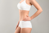 Young woman in underwear on grey background. Plastic surgery concept