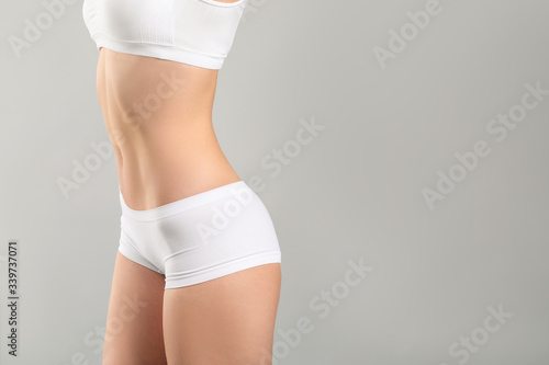 Young woman in underwear on grey background. Plastic surgery concept