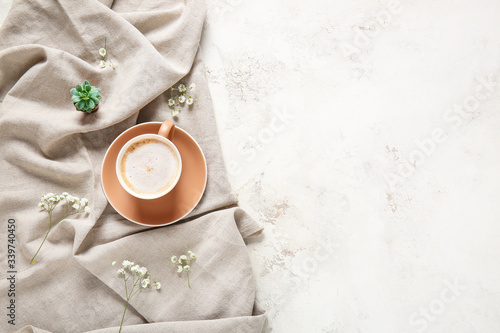 Cup of coffee, plaid and flowers on light background