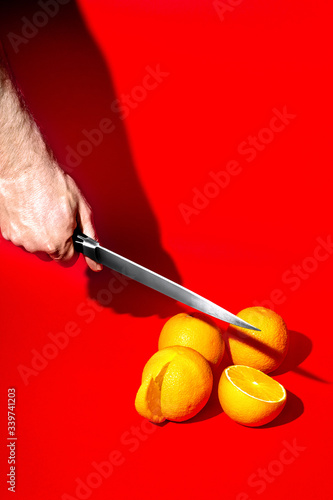 strong male hand slices juicy oranges. sharp knife. red background. fruit