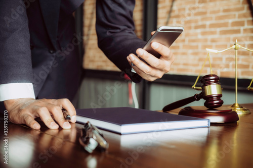 Justice and law concept. Gavel on sounding block in hand's Male judge at a courtroom, working with smart phone, report the case on table in modern office.