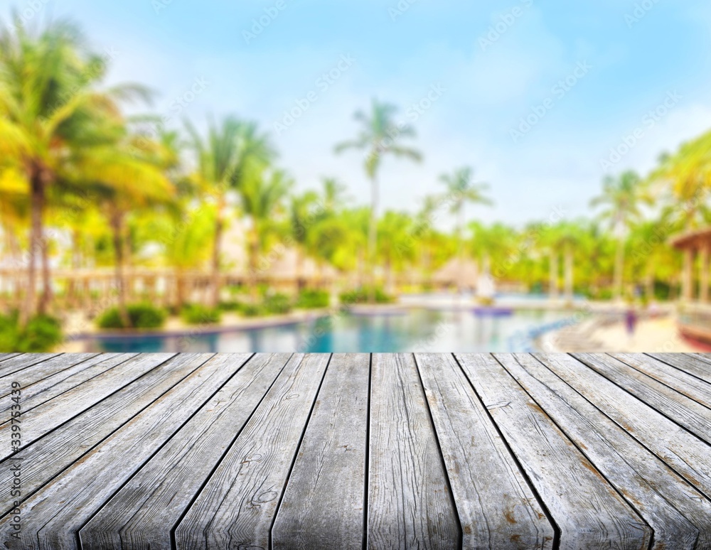 Empty wooden desk top with pool and palms on background Empty wooden desk top with pool and palms on background