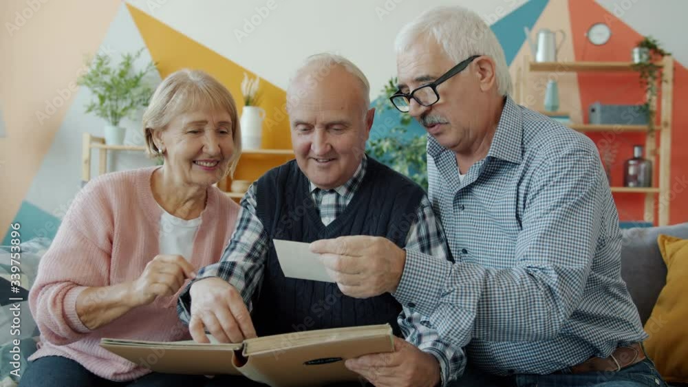 Slow motion of old men and woman friends watching pictures in photo album talking relaxing on couch at home. Friendship and memory concept. Slow motion of old men and woman friends watching pictures in photo album talking relaxing on couch at home. Friendship and memory concept.