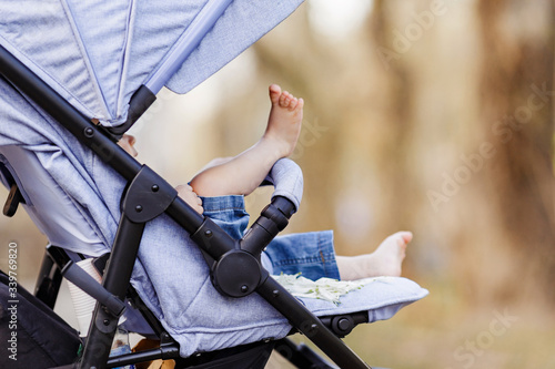 A little child under one year old is sitting in a blue stroller outside on a sunny day.