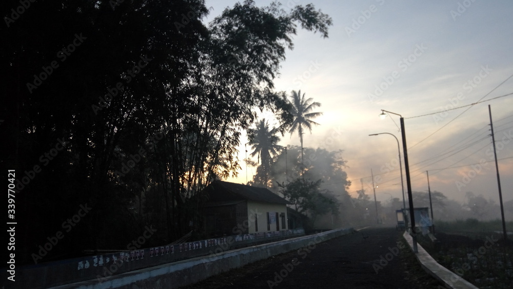 thin fog at sunrise in Kedu village, Central Java in Indonesia. a house on the edge of the village with trees and a road around it. This image contains motion noise, blurry, soft focus and poor lighti