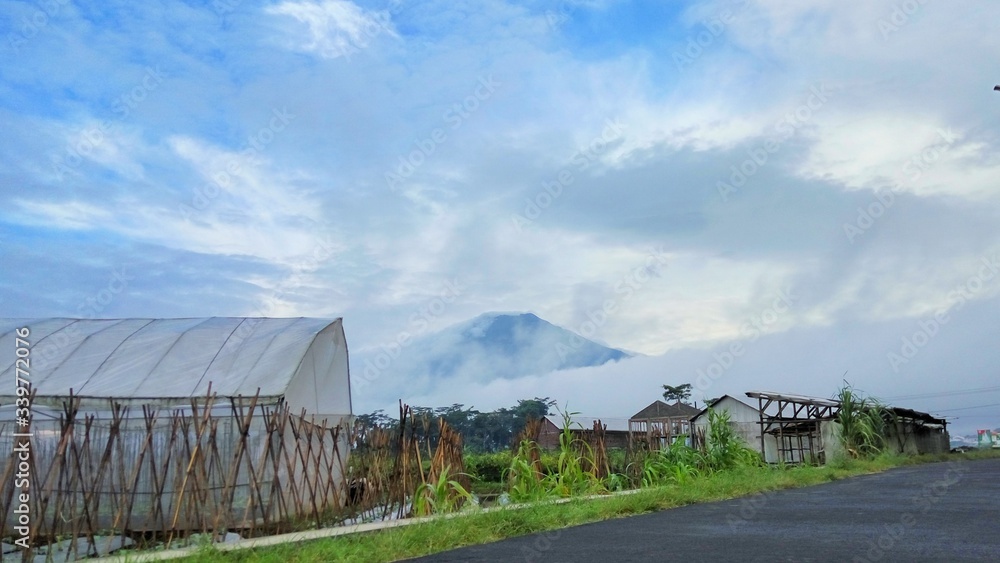 farmhouse in the countryside in the morning. fog, village road, Sumbing mountain and blue sky.