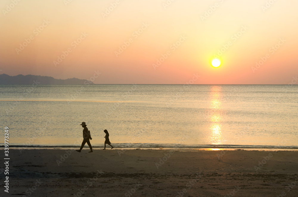 Mon and daughter walk together on the beach at sunset