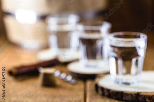Fototapeta Naklejka Na Ścianę i Meble -  Old rustic oak barrel and glasses of high quality distilled alcohol. Brazilian silver cachaça, called pinga, vodka, white rum, liqueur, pure drink, Poitín, sake, brandy or Absinthe.