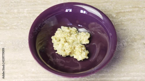 Metal spoon serving steaming hot oatmeal into a purple ceramic bowl on a plain table for breakfast