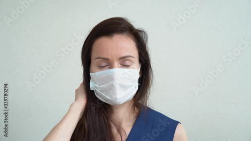 Beautiful Caucasian girl with long brown hair wear protective medical face mask raises her head, straightens her hair. Business woman looks directly at the camera close up. Isolated on gray background photo