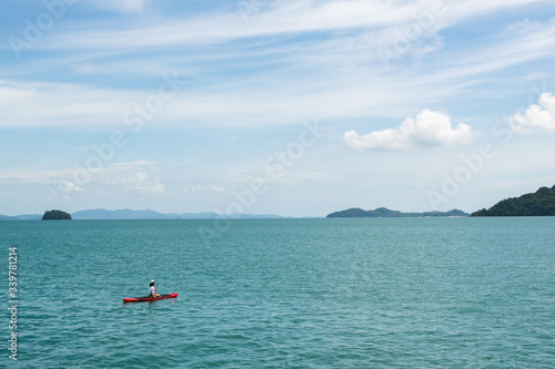 A woman kayaking on red kayak in emerald color water of Andaman sea with background of tropical island and copy space.