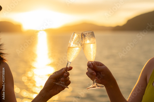 Women on yacht hold a glass of sparkling wine in her hand with background of golden sunset moment to celebrate her life and happiness. © 9mot