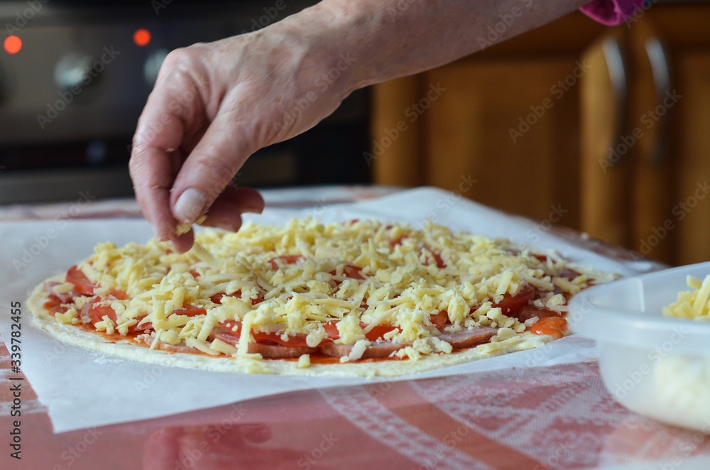 Cooking homemade Italian dishes. A woman's hand sprinkles grated cheese on an uncooked pizza