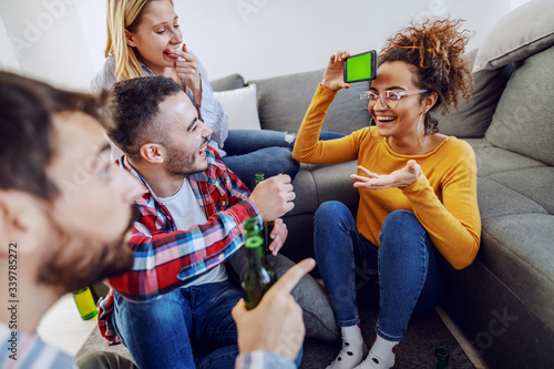 Group of cheerful playful friends playing charades with smart phone. Home interior.