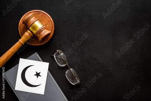 Islam sybmbol crescent and star near gavel and book on black table top view. Religious conflict concept. Copy space