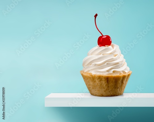 Cupcake with whipped cream and cherry on the desk