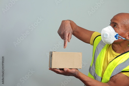 COVID-19 Coronavirus pandemic global outbreak delivery man with parcel and dust face mask fighting the disease on grey background 