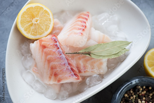 Close-up of raw fresh codfish fillet on ice with bay leaves and lemon, selective focus, studio shot