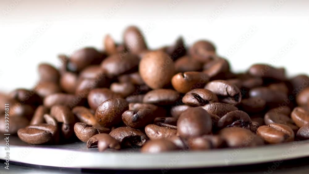 Pouring cup of roasted golden brown coffee beans on top of round silver scale. Pouring cup of roasted golden brown coffee beans on top of round silver scale.