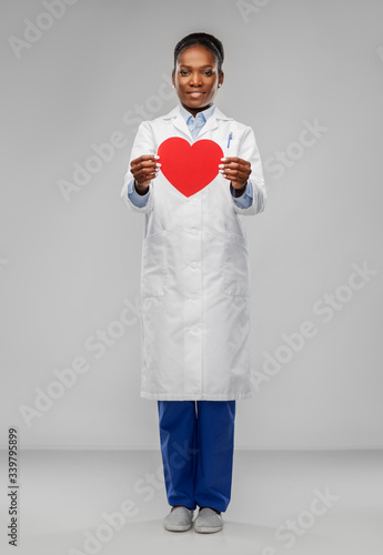 medicine, cardiology and healthcare concept - smiling african american female doctor in white coat with red heart over grey background © Syda Productions