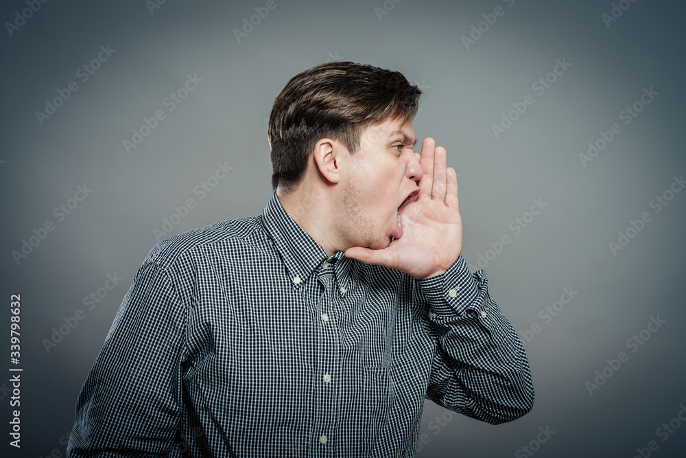 Closeup side view profile portrait, angry upset young man, worker, employee, business man, hand to mouth, open mouth yelling, isolated white background. Negative emotion facial expression emotion Closeup side view profile portrait, angry upset young man, worker, employee, business man, hand to mouth, open mouth yelling, isolated white background. Negative emotion facial expression emotion