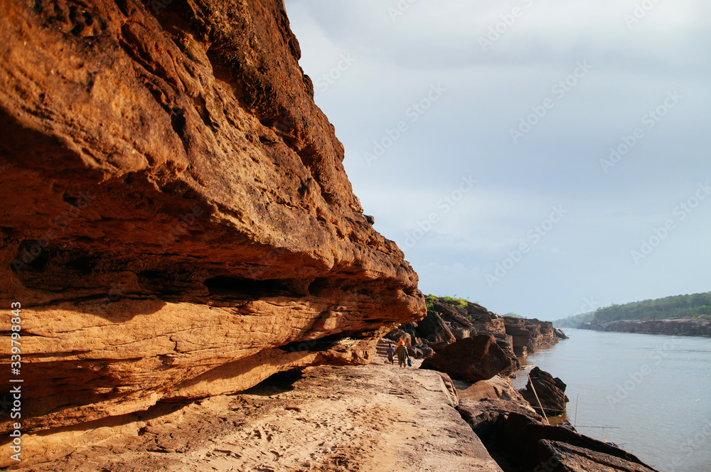Large Sand stone canyon cliff shoreline of Mekong river and local peoples walking along