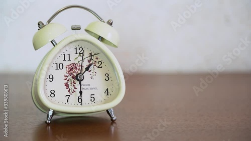 White retro alarm o-clock with bells stand on a brown wood table on blurred background close up. Classic old bell shows about 1.30 p.m. Second hand moving very fast on the clock face, accelerated