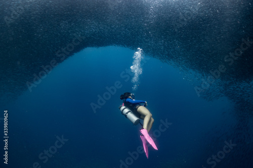 A female scuba diver diving with millions of fish in the Philippines.