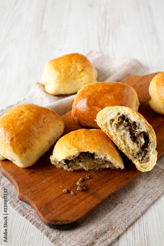 Home-baked Beef Russian Bierocks on a rustic wooden board on a white wooden table, low angle view. Copy space. Home-baked Beef Russian Bierocks on a rustic wooden board on a white wooden table, low angle view. Copy space.