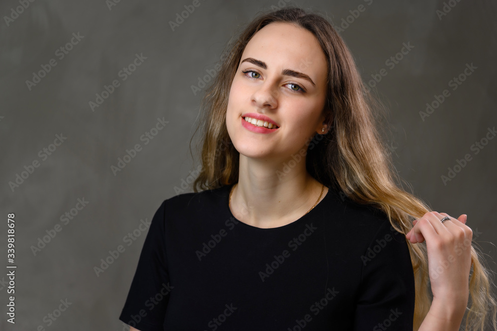 Portrait Caucasian happiness girl in a black dress with long hair and a beautiful smile on a gray background. Portrait Caucasian happiness girl in a black dress with long hair and a beautiful smile on a gray background.