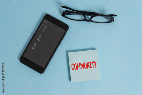 Word writing text Community. Business photo showcasing group of showing with a common characteristics living together Dark eyeglasses colored sticky note smartphone fashion pastel background photo